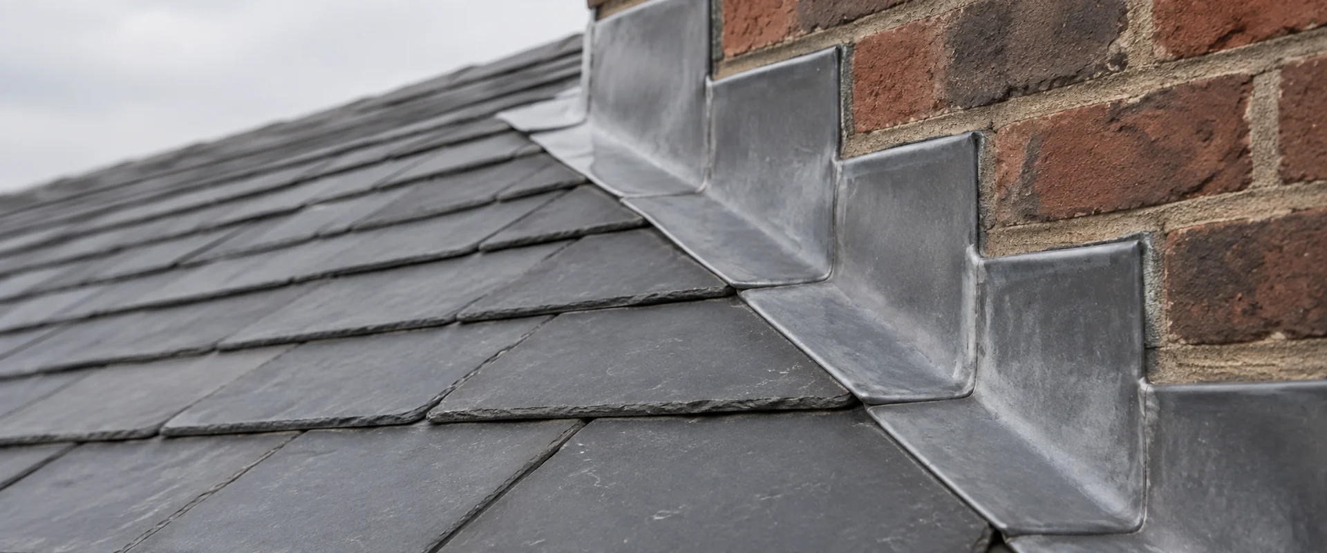 Illustrative stepped lead flashing beside brickwork on a slate roof.