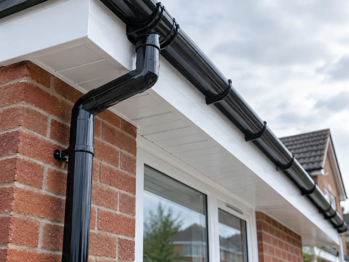 White soffit boards with black guttering and downpipe on a brick house.